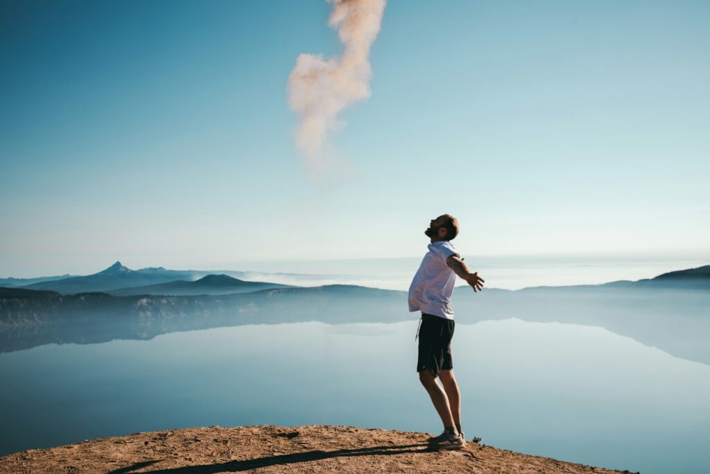 A happy man with arms outstretched, view of a lake and mountains in the distance