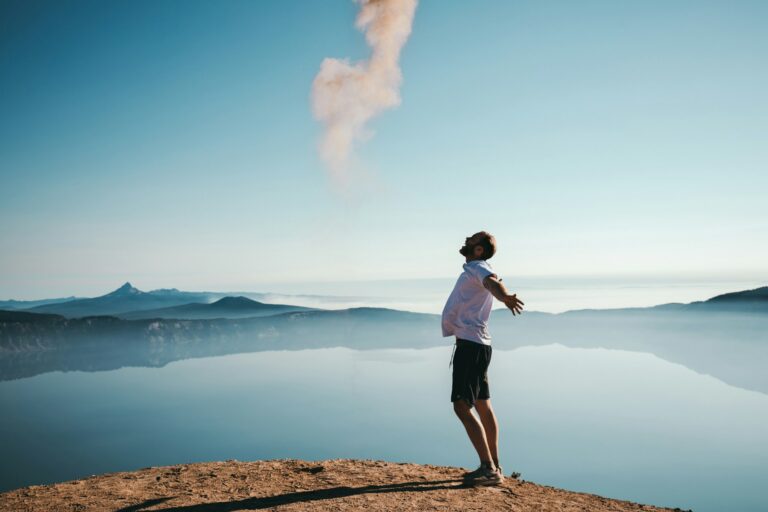 A happy man with arms outstretched, view of a lake and mountains in the distance