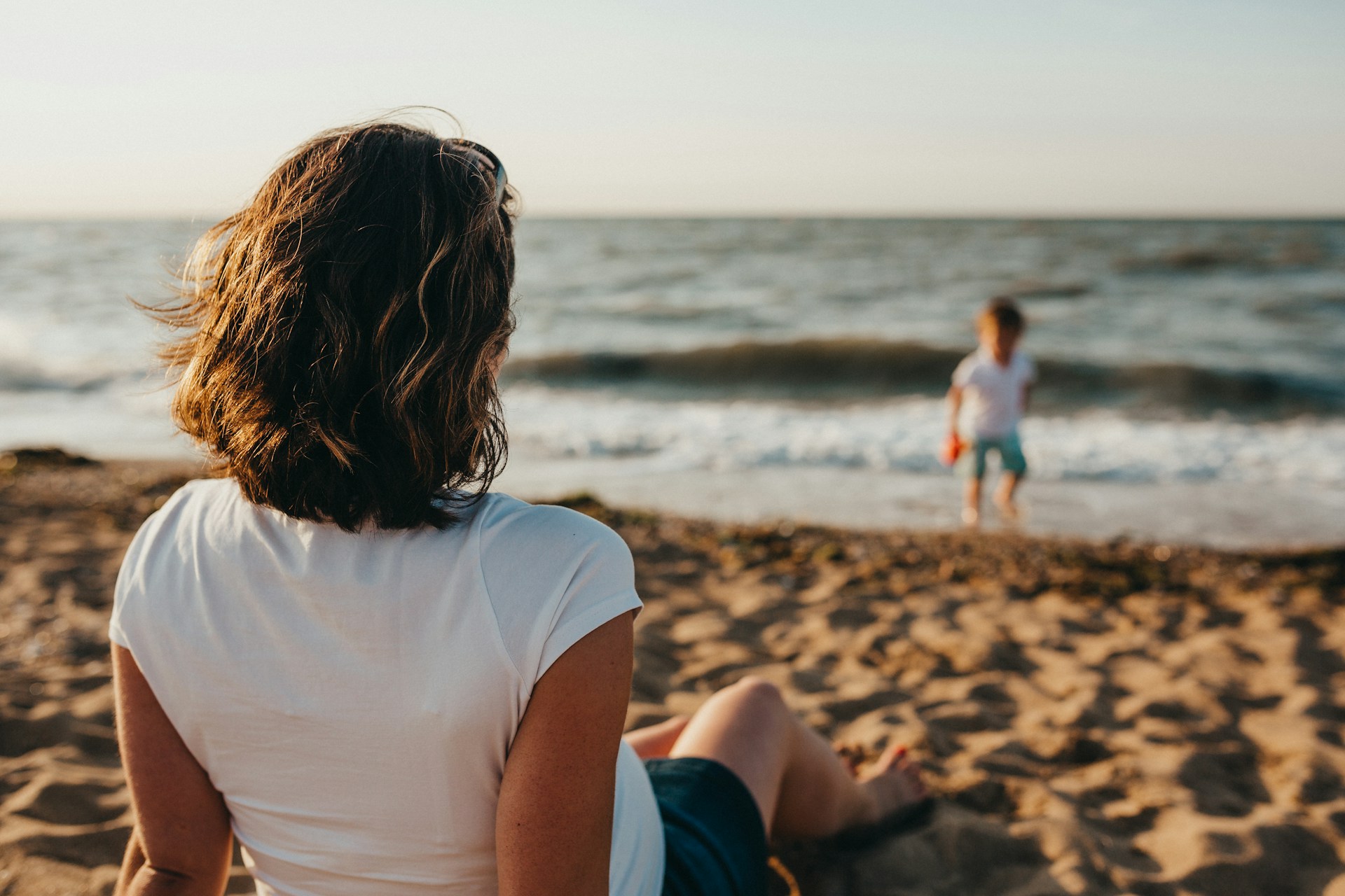 Mom sitting on the beach, looking at her young child